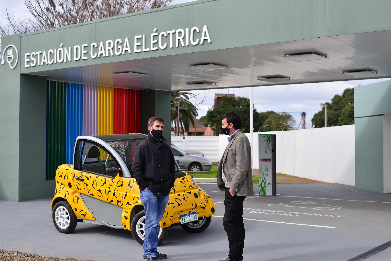 Un vehículo eléctrico y dos personas frente a una estación de carga